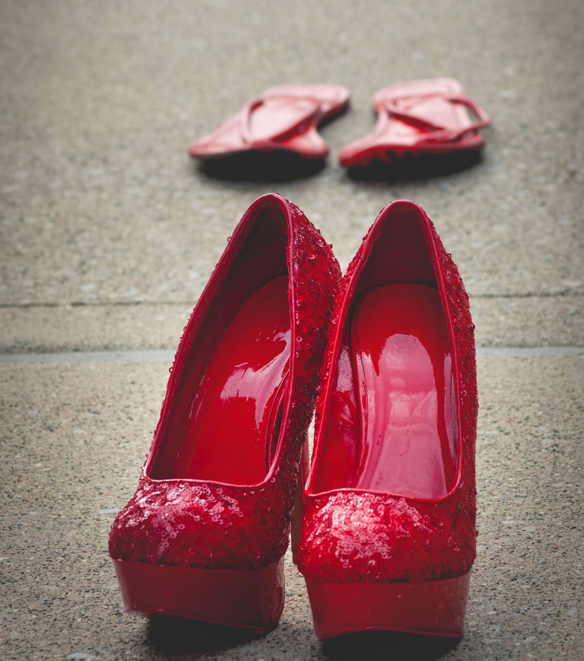 Pair of sequin heels painted red, sitting on pavement in courtyard